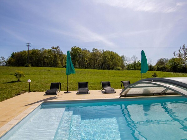 A swimming pool with four lounge chairs and two umbrellas, surrounded by a grassy area and trees.