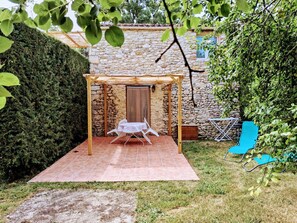A patio with a pergola, a stone wall, and a small table and chairs.