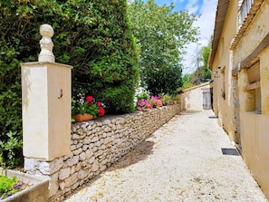 A narrow stone pathway leading to a building with a stone wall and potted plants.