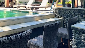A poolside area with lounge chairs, a stone wall, and a tree. - Pandawa Villa Riverside by WizZeLa (Tabanan)