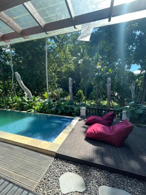 A pool area with a wooden deck, red cushions, and a glass ceiling. - Pandawa Villa Riverside by WizZeLa (Tabanan)