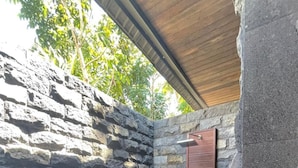 A stone wall, a wooden door, and a small wooden platform with plants. - Pandawa Villa Riverside by WizZeLa (Tabanan)