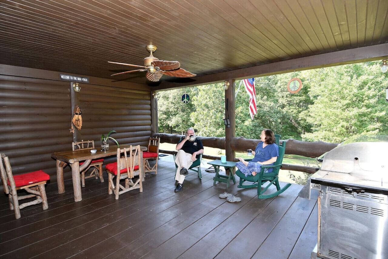 Un espace extérieur abrité, doté d’une table et de chaises en bois, d’un ventilateur de plafond et d’un barbecue.