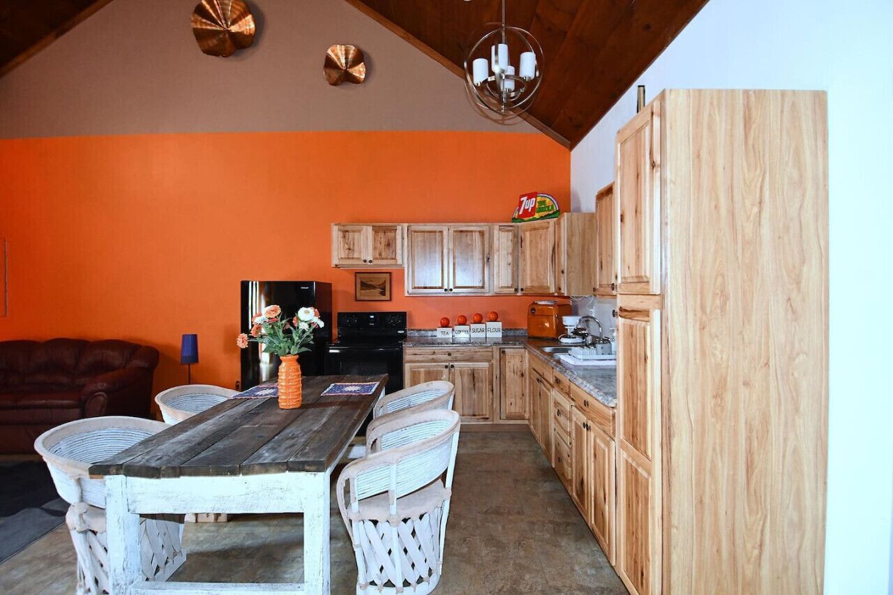Une cuisine avec des meubles en bois, une table à manger avec des chaises et un lustre.