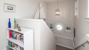 A staircase with a white railing, a bookshelf with books, a small sailboat decoration, and a wall-mounted light fixture. - Coastal Retreat at The Rookery: 4 BDRM Home (Pawleys Island)