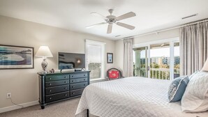 A bedroom with a bed, a dresser, a ceiling fan, a TV, and a window with curtains. - Coastal Retreat at The Rookery: 4 BDRM Home (Pawleys Island)