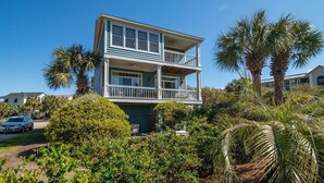 A two-story building with a balcony on the upper floor, surrounded by lush greenery and palm trees. - Coastal Retreat at The Rookery: 4 BDRM Home (Pawleys Island)