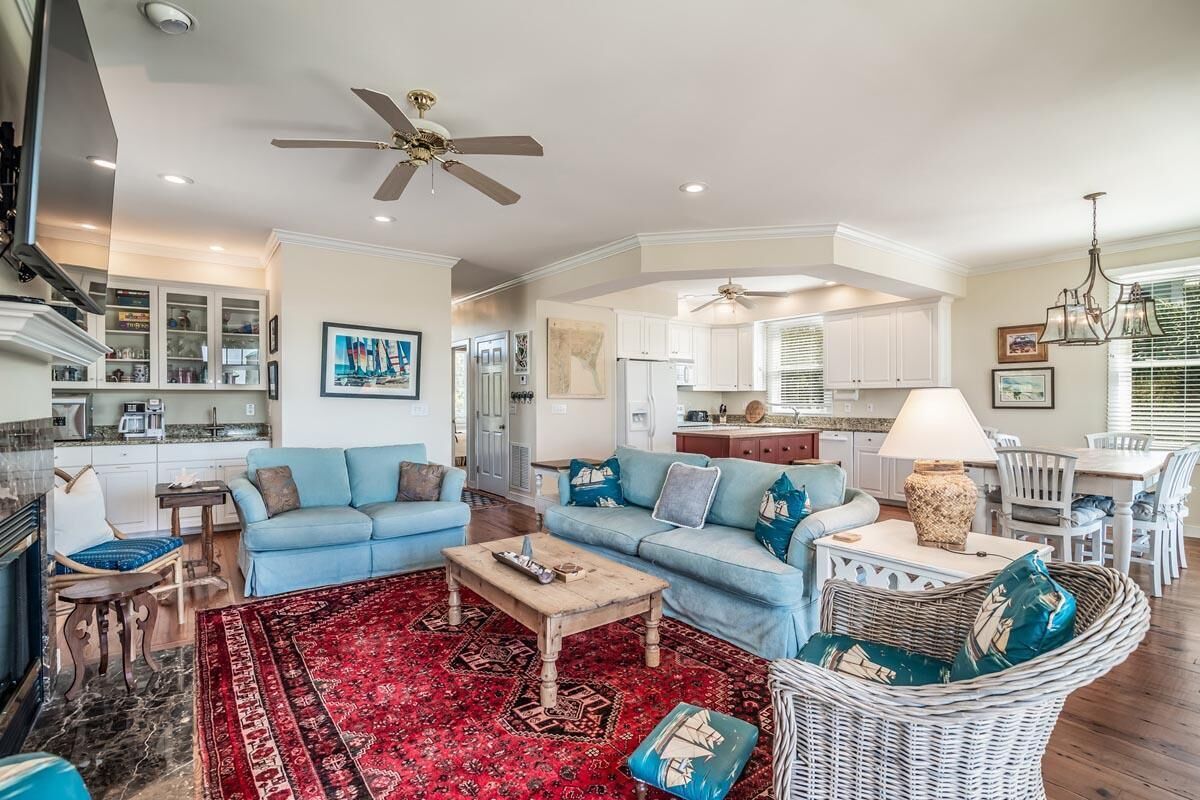 A spacious living room with a red patterned rug, a blue sofa set, and a wicker chair.