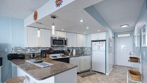 A modern kitchen with white cabinets, granite countertops, stainless steel appliances, and a central island with stools. - Beautiful sunset and ocean view from 2 Bedroom Condo with Free WiFi and an Outdoor Pool Located in Midtown Only Steps to Beach! Vacation at the Shore with Shoreline Properties (Ocean City)