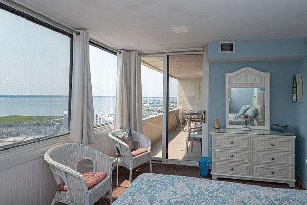 A hotel room with a balcony, a bed, a dresser, and a chair.