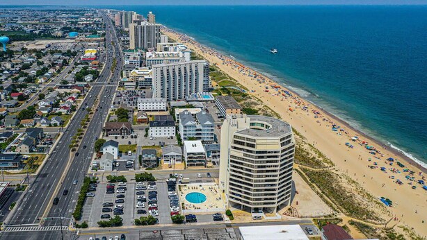 An aerial view of a coastal city with a beachfront hotel, a parking lot, and a clear view of the ocean. - Beautiful sunset and ocean view from 2 Bedroom Condo with Free WiFi and an Outdoor Pool Located in Midtown Only Steps to Beach! Vacation at the Shore with Shoreline Properties (Ocean City)