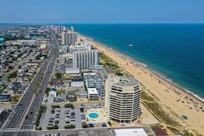 An aerial view of a coastal city with a beachfront hotel, a parking lot, and a clear view of the ocean.