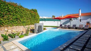 Ein rechteckiger Pool mit Steinbord, umgeben von Liegestühlen und einer Steinmauer mit einer grünen Hecke.