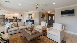 Una sala de estar moderna con un sofá, sillones y una mesita de centro. Se ve una cocina al fondo.