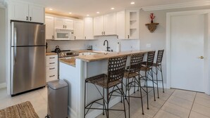 Cocina moderna con armarios blancos, refrigerador de acero inoxidable, microondas y una pileta con taburetes de bar.