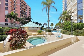 A pool area with a small gazebo, palm trees, and a multi-story building in the background. - Beachfront Condo Building | Pool, Tennis & Views (Marco Island)
