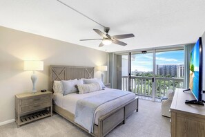 A bedroom with a bed, nightstands, a desk, a ceiling fan, and a large window with a city view.