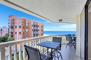 A balcony with a table and chairs, overlooking a beach and a pink building.