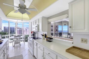 A modern kitchen with white cabinets, a ceiling fan, and a large window overlooking a cityscape.