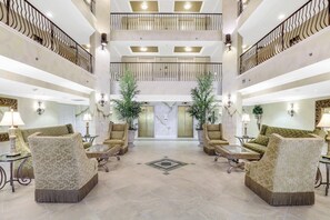 A spacious lobby with a high ceiling, two levels of balconies, and a central seating area with sofas and tables.