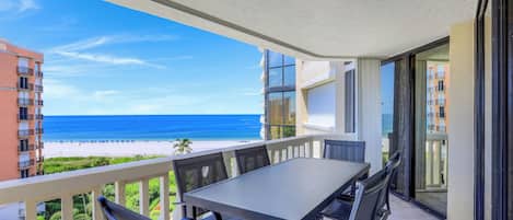A balcony with a table and chairs, overlooking a beach and ocean.