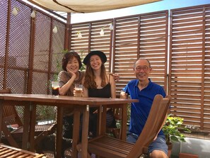 A wooden outdoor seating area with a table and chairs, surrounded by a wooden fence and a pergola with string lights. - Y's B&Kitchen Tokyo HY1 (Tokyo)