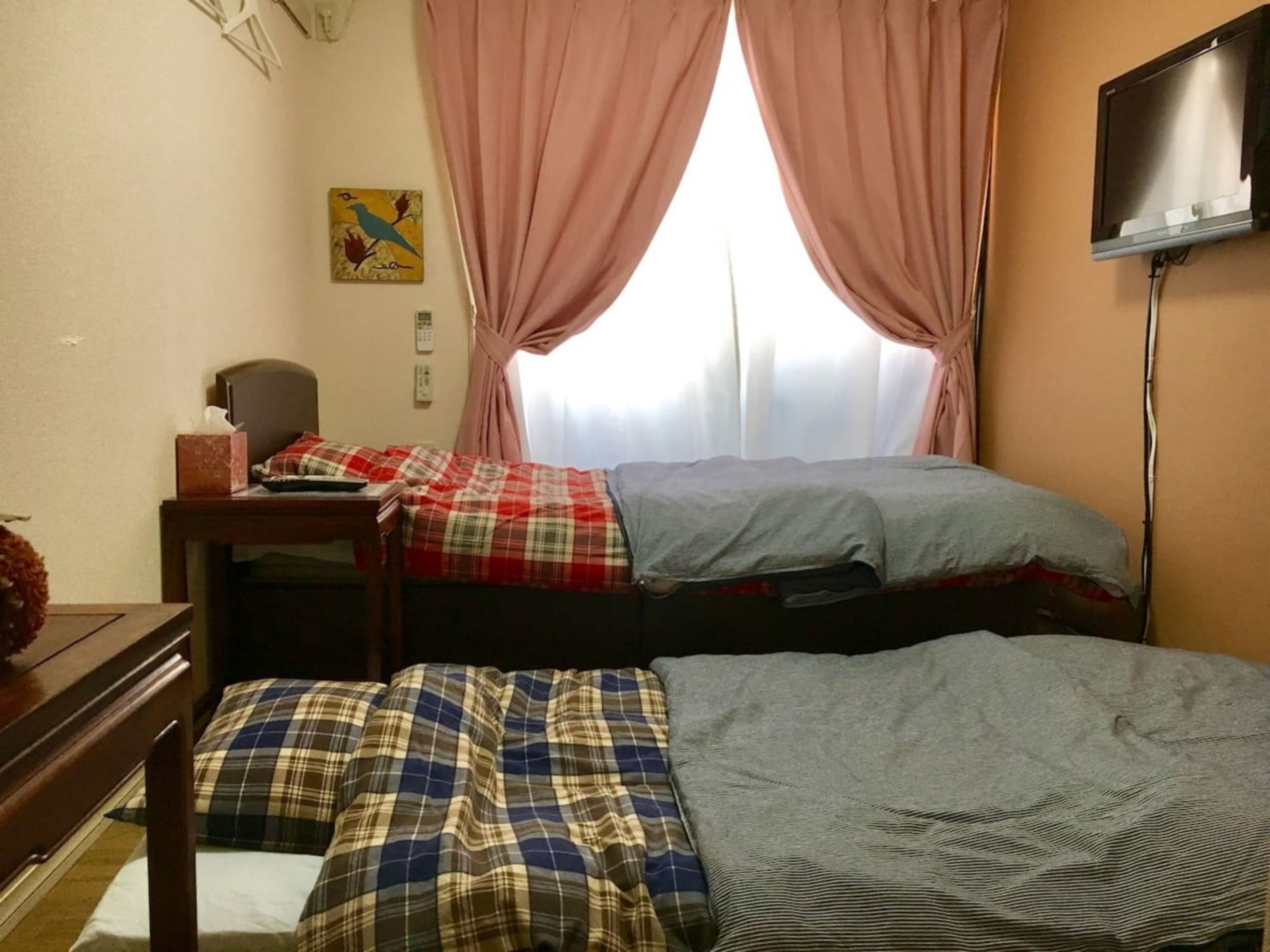 Una habitación con dos camas, un escritorio, una silla, un televisor y una ventana con cortinas.