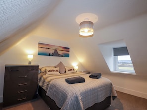 A bedroom with a bed, a dresser, a painting, a window, and a ceiling light fixture. - Nanville (Beauly)