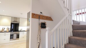 A kitchen with white cabinets, a stainless steel range hood, and a wooden coat rack with hooks. - Nanville (Beauly)