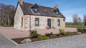 A stone house with a pitched roof, two chimneys, and a gravel driveway. - Nanville (Beauly)