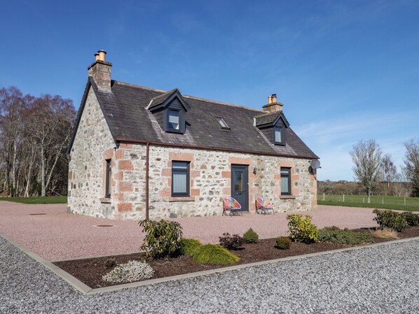 A stone house with a pitched roof, two chimneys, and a gravel driveway. - Nanville (Beauly)