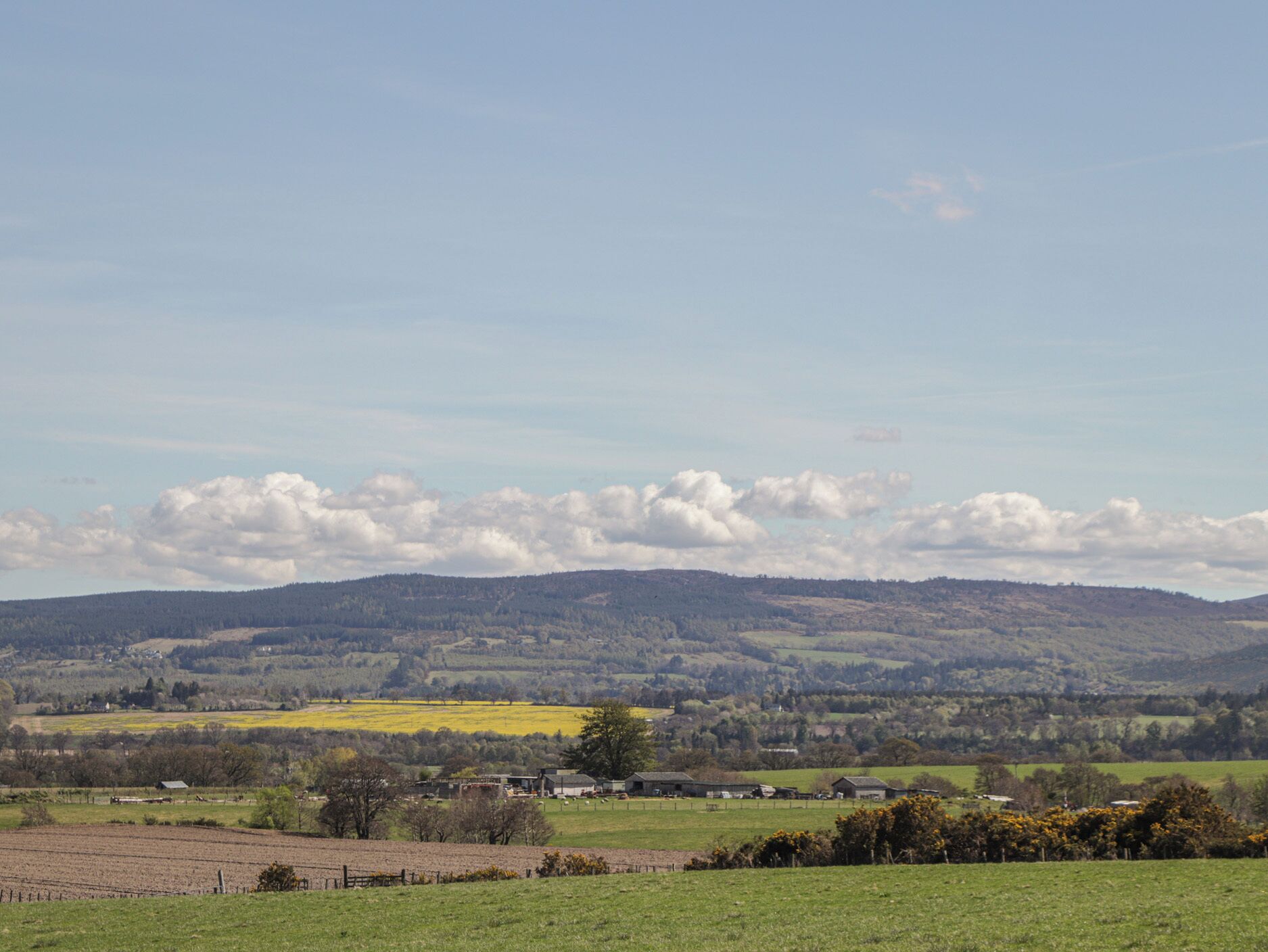 Een landelijk landschap met glooiende heuvels, een heldere lucht en verspreide gebouwen.
