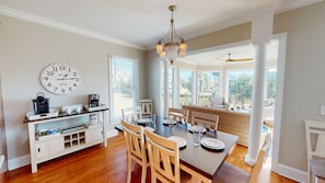 A dining area with a wooden table, chairs, a chandelier, a clock, and a coffee station.