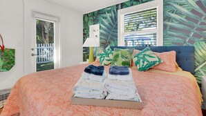 Una cama bien hecha con toallas dobladas, un cabecero azul y papel tapiz tropical.