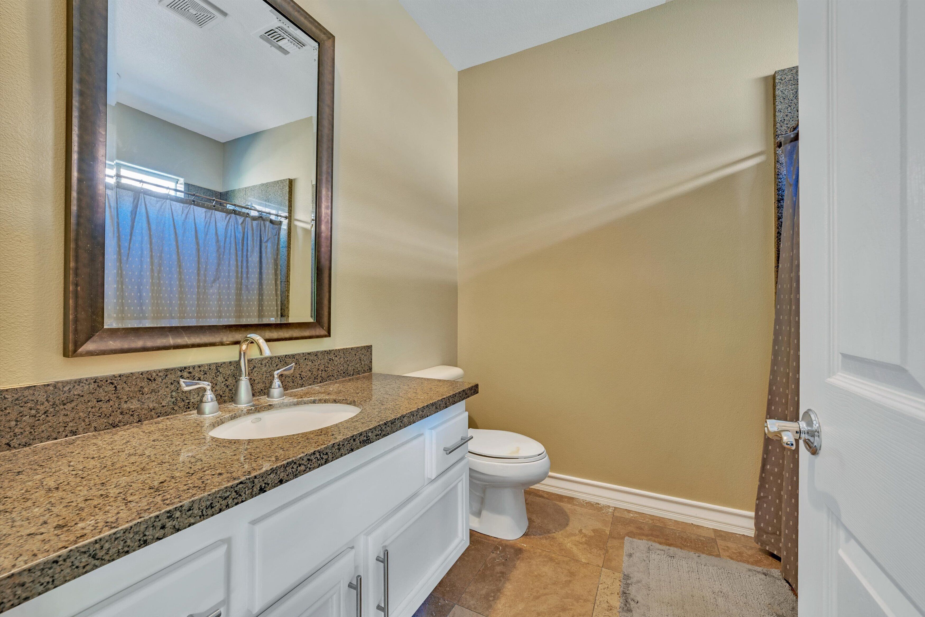 A bathroom with a granite countertop sink, a white toilet, and a large mirror.