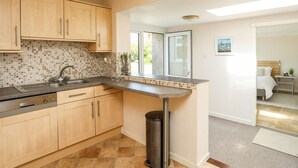 A modern kitchen with wooden cabinets, a tiled backsplash, a stainless steel sink, and a trash can. - Ty Bedw (Tyn-y-Gongl)