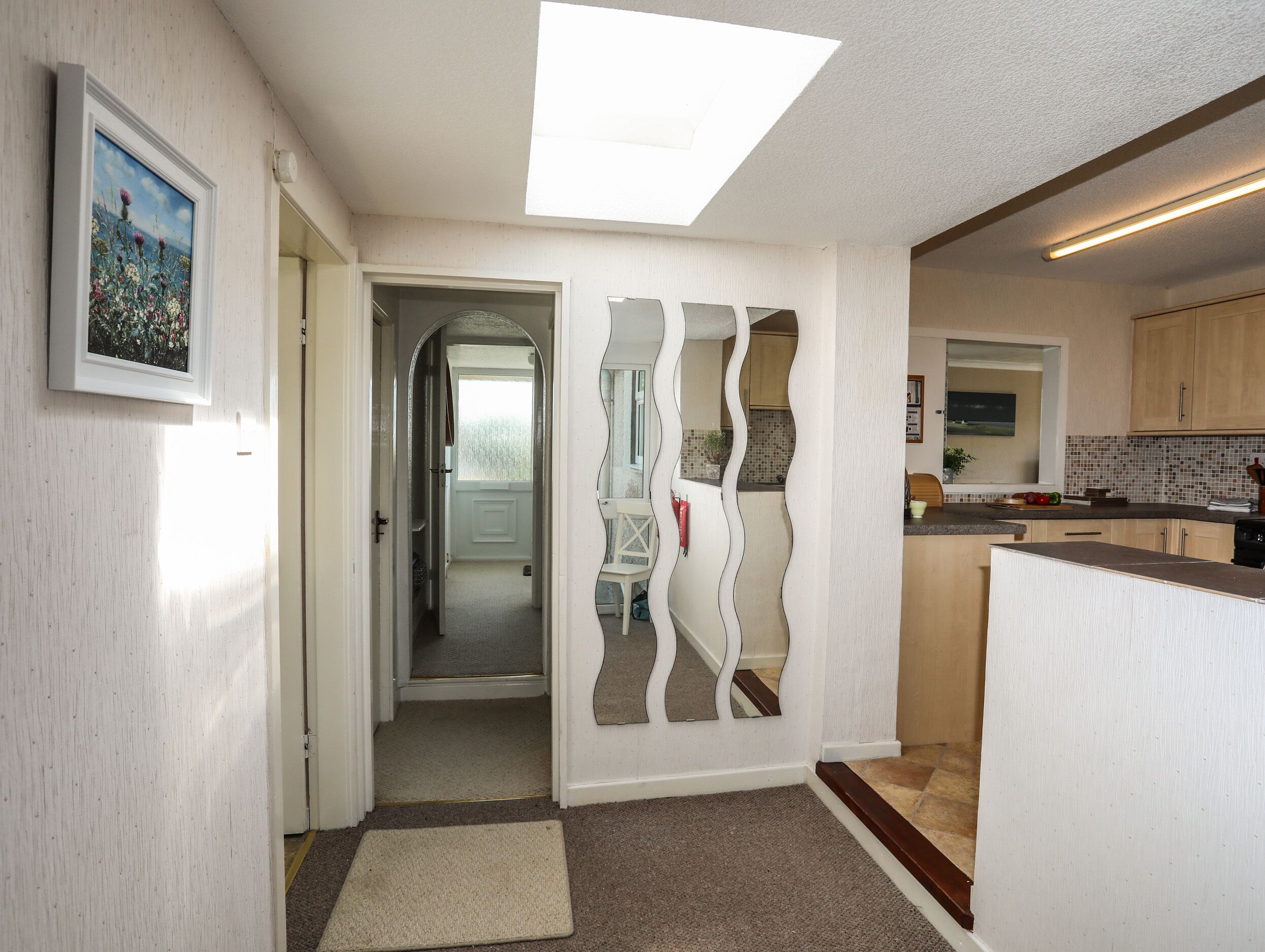 A hallway with a door leading to a bedroom, a kitchen area with wooden cabinets, and a ceiling light fixture.