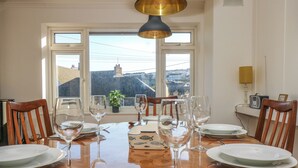 A dining table set with plates, wine glasses, and cutlery, with a view of a cityscape through large windows. - Rock Pool House (Helston)