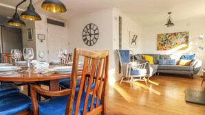 A dining area with a wooden table set for four, a blue upholstered chair, and a modern light fixture above. - Rock Pool House (Helston)