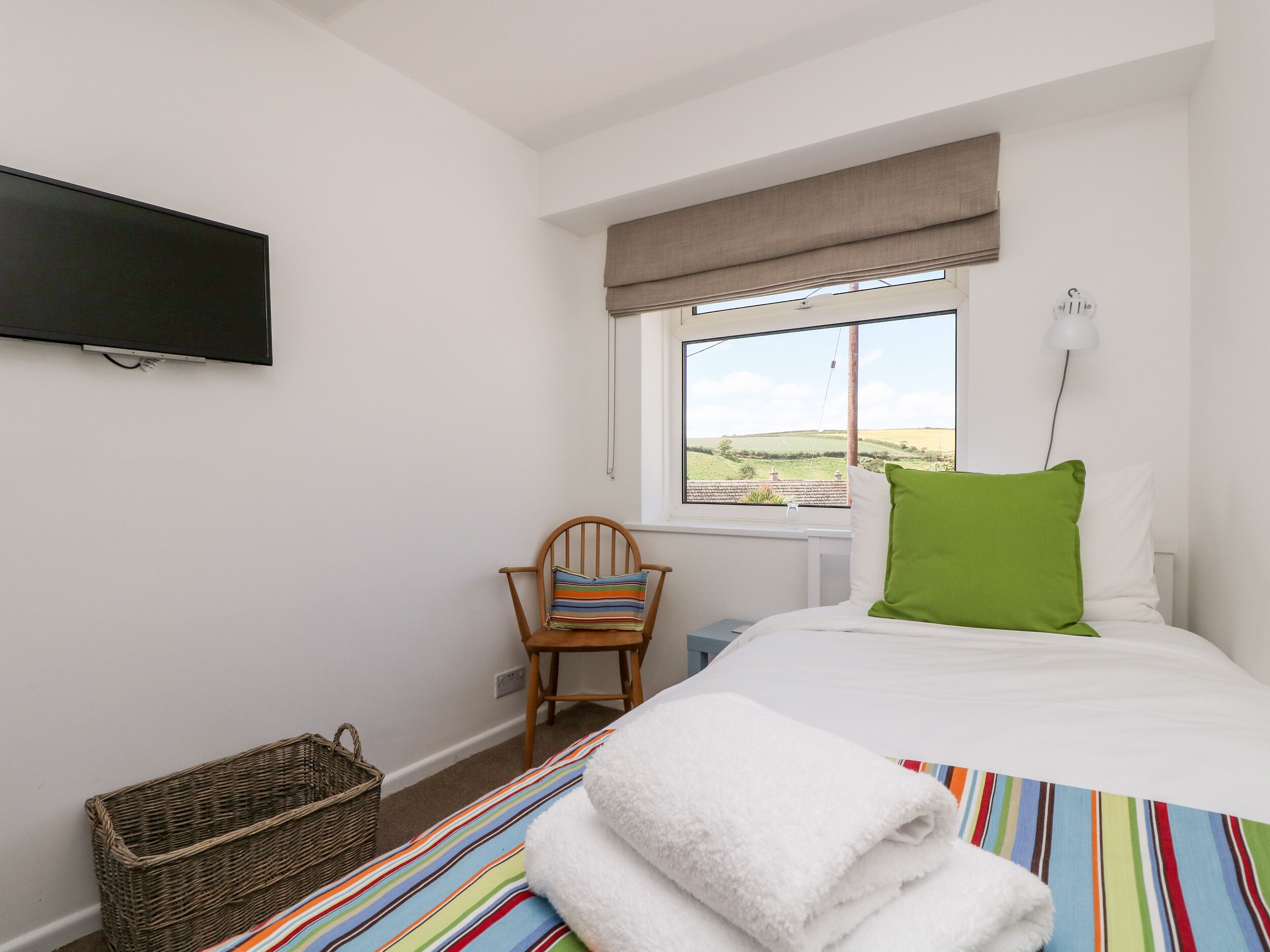 Une chambre à coucher avec un lit, une chaise, une télévision, une fenêtre et un panier.