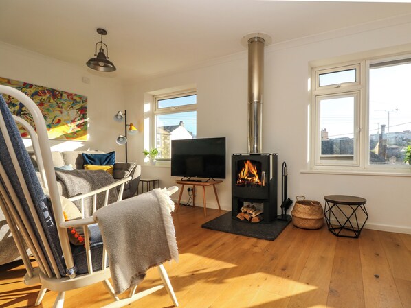 A cozy living room with a fireplace, wooden flooring, a TV, and a view of the city through large windows.
