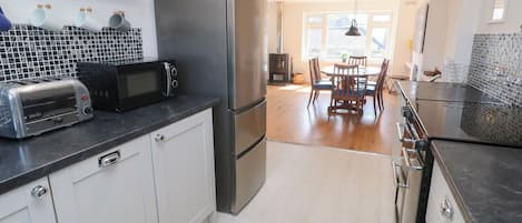 A modern kitchen with stainless steel appliances, a dining area with a table and chairs, and a view of the outdoors through large windows.