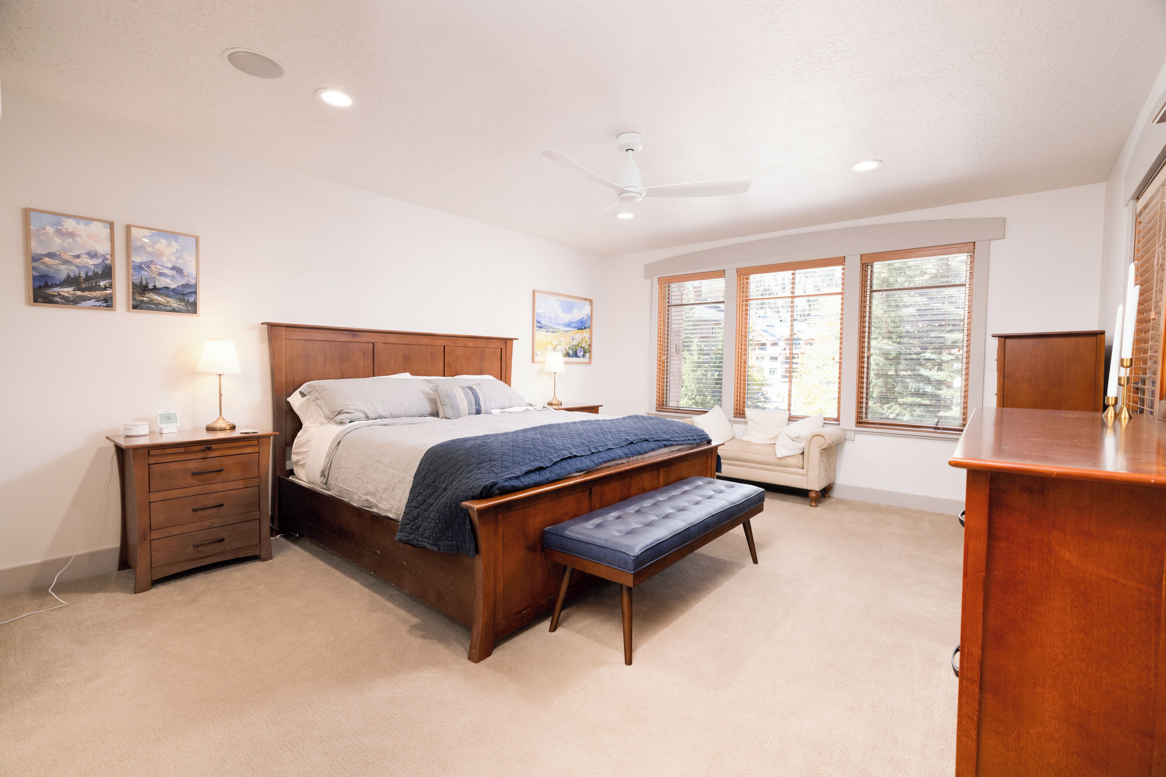 A bedroom with a wooden bed, a bench, a nightstand, and a dresser.