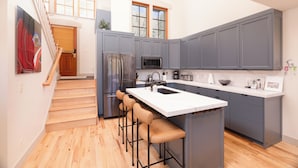 A modern kitchen with grey cabinets, a white countertop, and a stainless steel refrigerator. There is a wooden staircase leading to an upper level. - First Tracks (with AC unit!) by Cottonwood Lodging (Solitude)