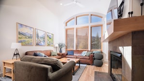 A living room with a fireplace, leather sofas, wooden coffee table, and large windows with blinds. - First Tracks (with AC unit!) by Cottonwood Lodging (Solitude)