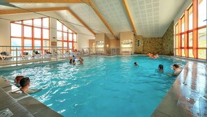 Una piscina interior con paredes de vidrio transparente, vigas de madera y muros de piedra.