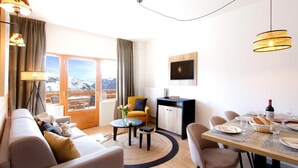 Una habitación de hotel moderna con sofá, mesa de comedor y vistas a montañas a través de amplias ventanas.