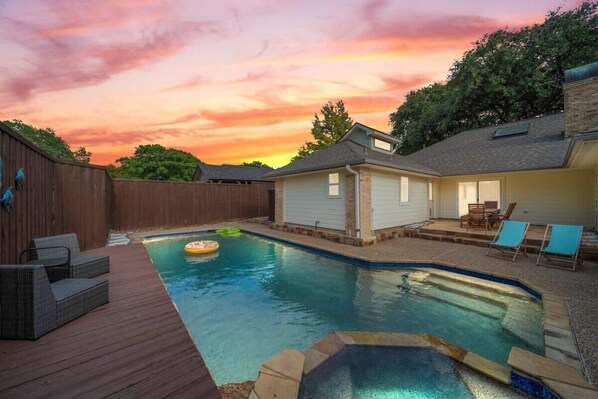 Un patio trasero con piscina, sillas de deck y un jacuzzi.