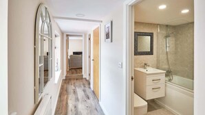 A hallway leading to a bathroom with a shower, a sink, and a mirror. - Host & Stay | Lobster Pot Apartment (Whitby)