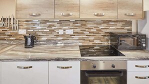 A modern kitchen with wooden cabinets, a tiled backsplash, a built-in oven, and a coffee maker. - Host & Stay | Lobster Pot Apartment (Whitby)